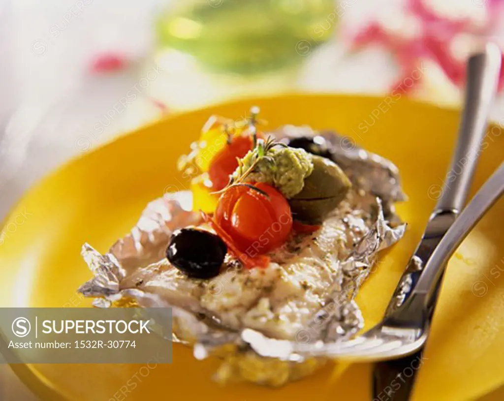 Fish fillet with pesto, tomatoes & olives on aluminium foil