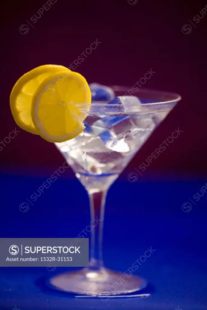 A glass of Martini with ice cubes and lemon slices