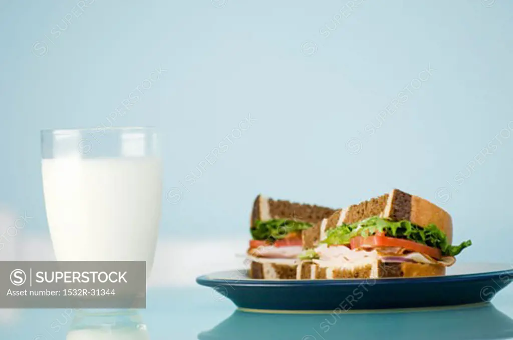 A glass of milk and a sandwich in marble bread