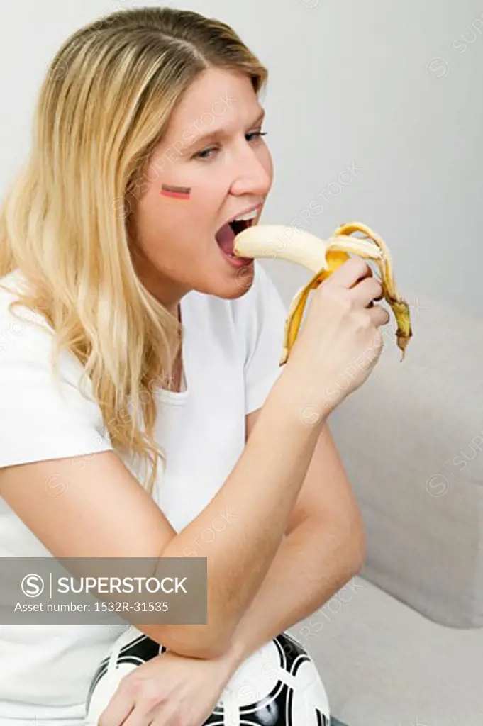 Young woman with football eating a banana
