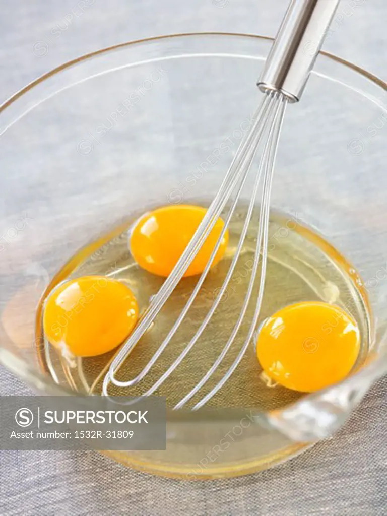 Three eggs broken into a glass bowl with whisk