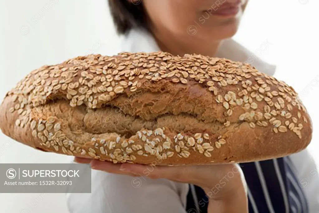 Woman holding a loaf of oat bread on the flat of her hand