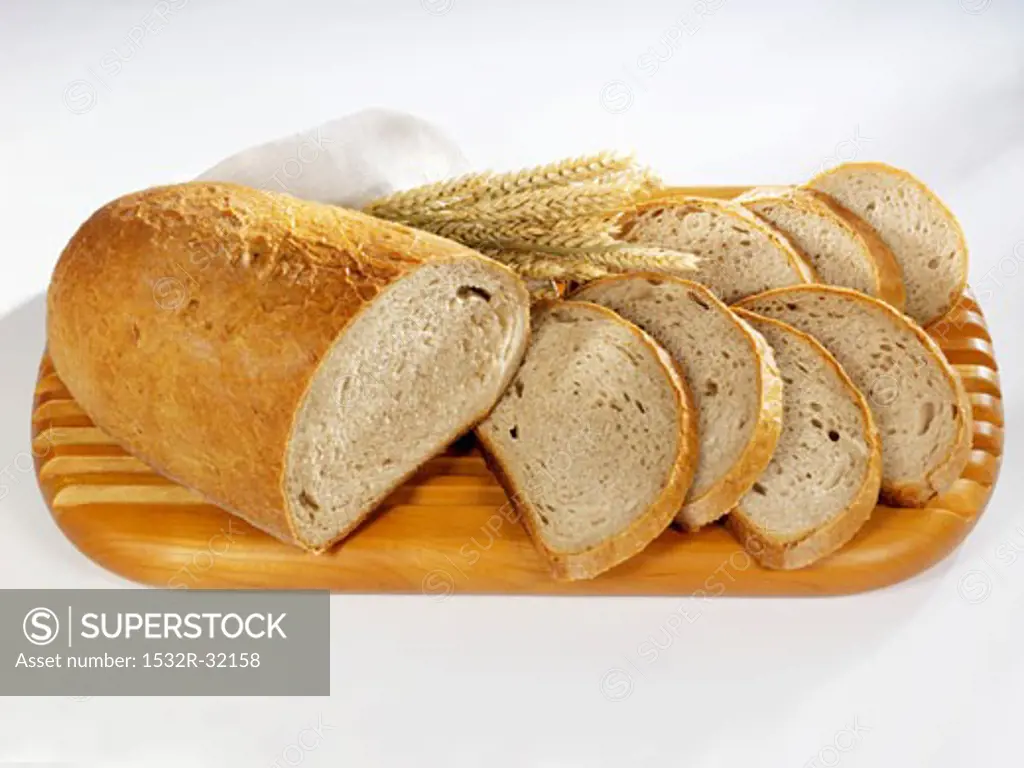 Partly sliced loaf of bread on a wooden board