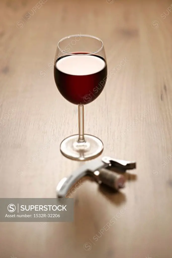 A glass of red wine with corkscrew and cork