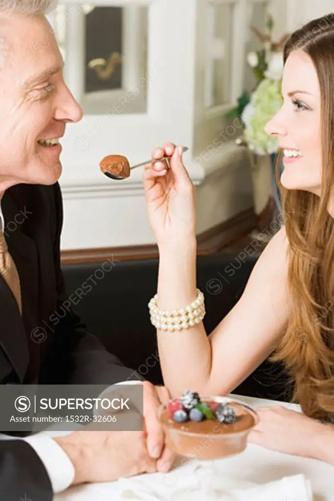 Woman offering man spoonful of chocolate cream in restaurant