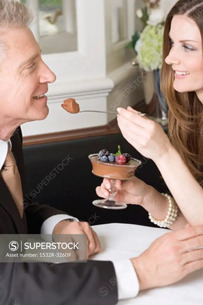 Woman offering man spoonful of chocolate cream in restaurant