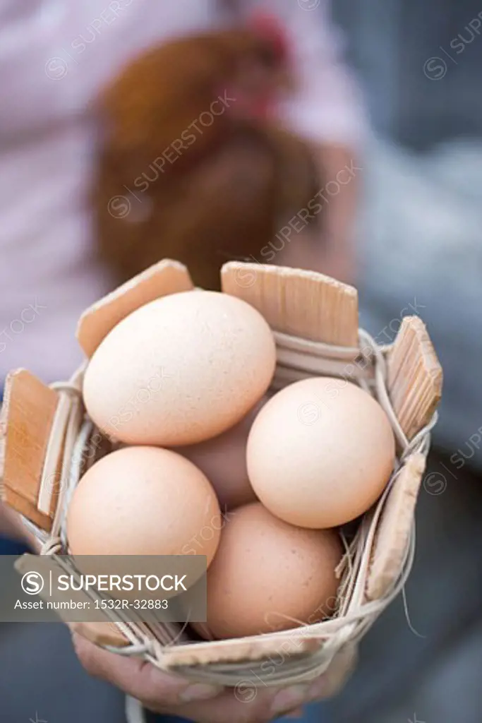 Woman holding basket of eggs and live hen