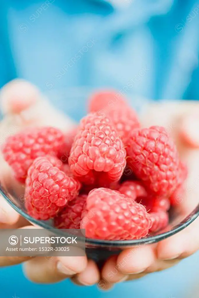 Child's hands holding glass dish of raspberries