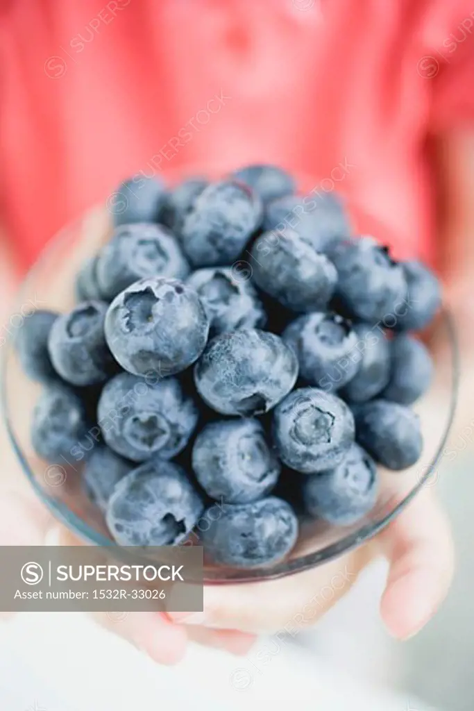 Child's hands holding glass dish of blueberries