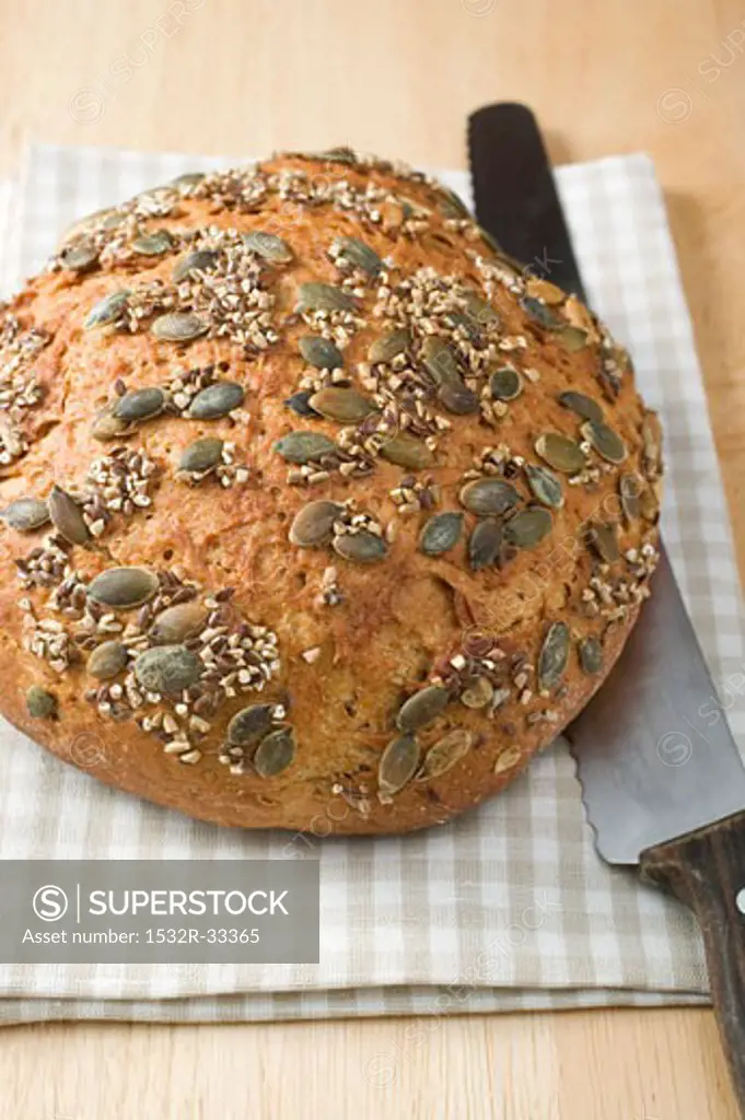 Wholemeal bread with pumpkin seeds on tea towel with bread knife