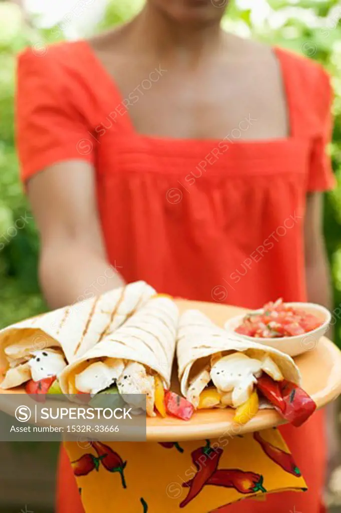 Woman holding plate of wraps and salsa