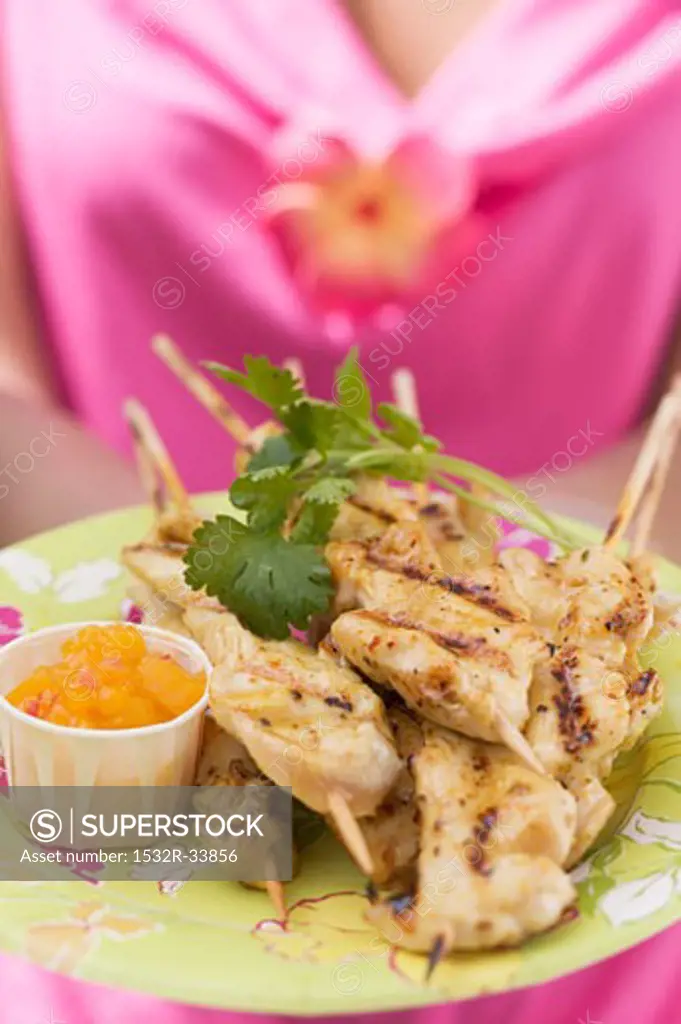 Woman holding plate of satay and chutney