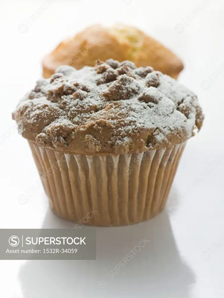 Nut muffin sprinkled with icing sugar in front of lemon muffin