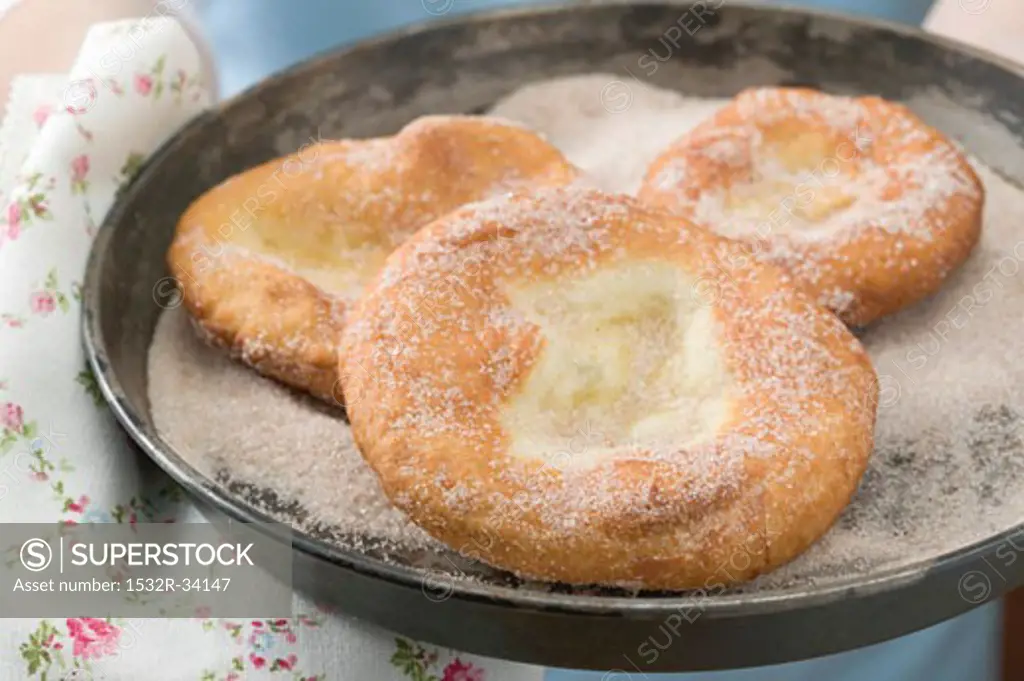 Hands holding Auszogene (Bavarian doughnuts) in frying pan