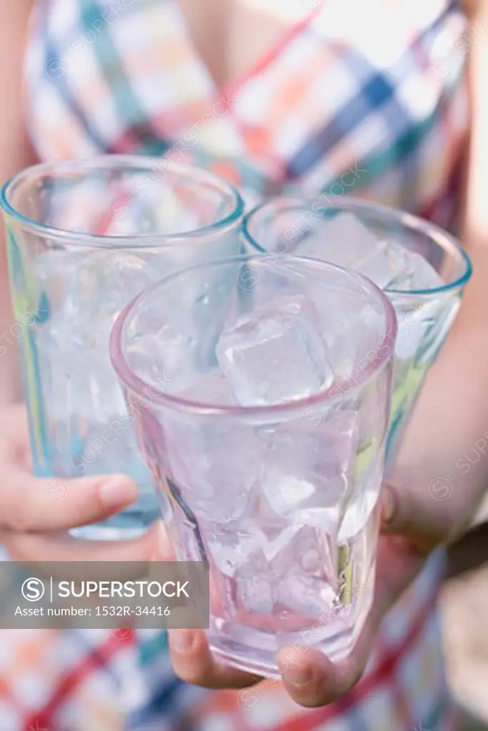 Woman holding three glasses filled with ice cubes