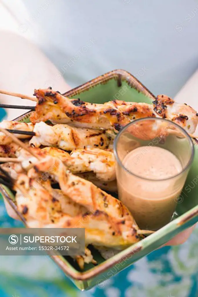 Woman holding grilled satay with dip