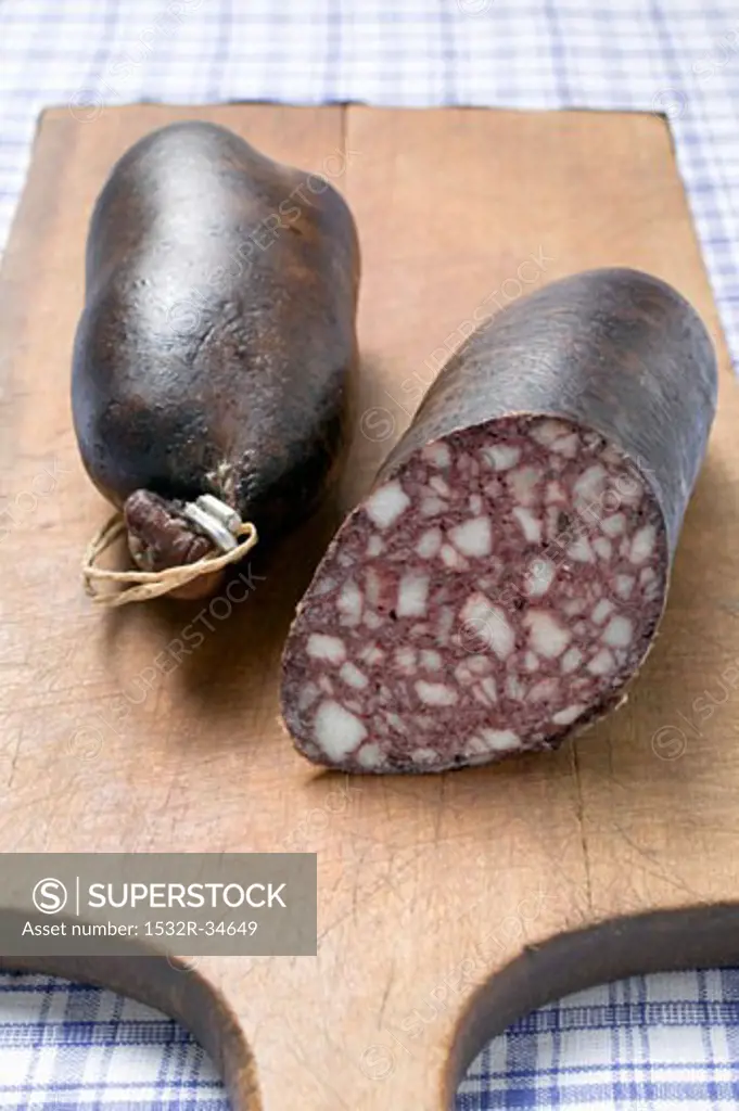 Two black puddings on chopping board, one with a piece removed