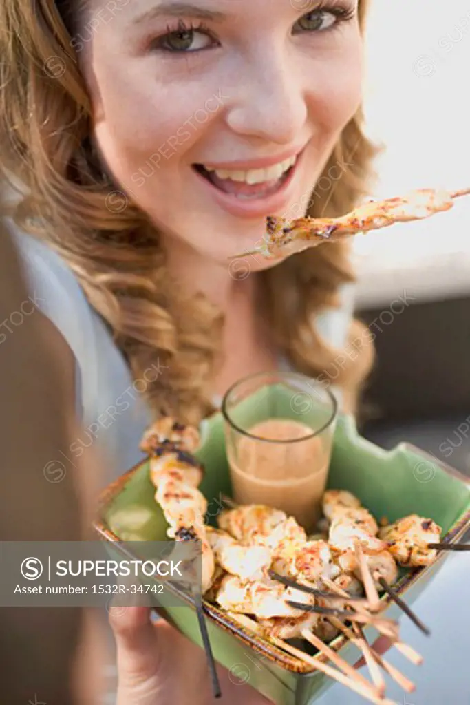 Woman eating grilled satay with peanut dip