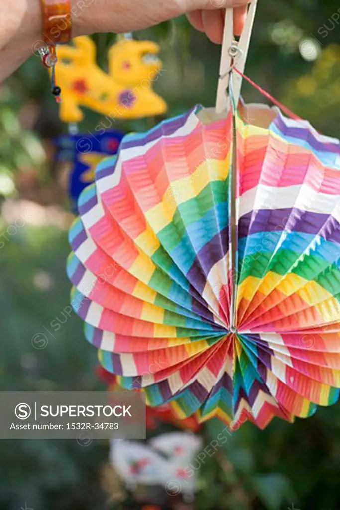 Hand hanging coloured Chinese lantern on washing line in garden