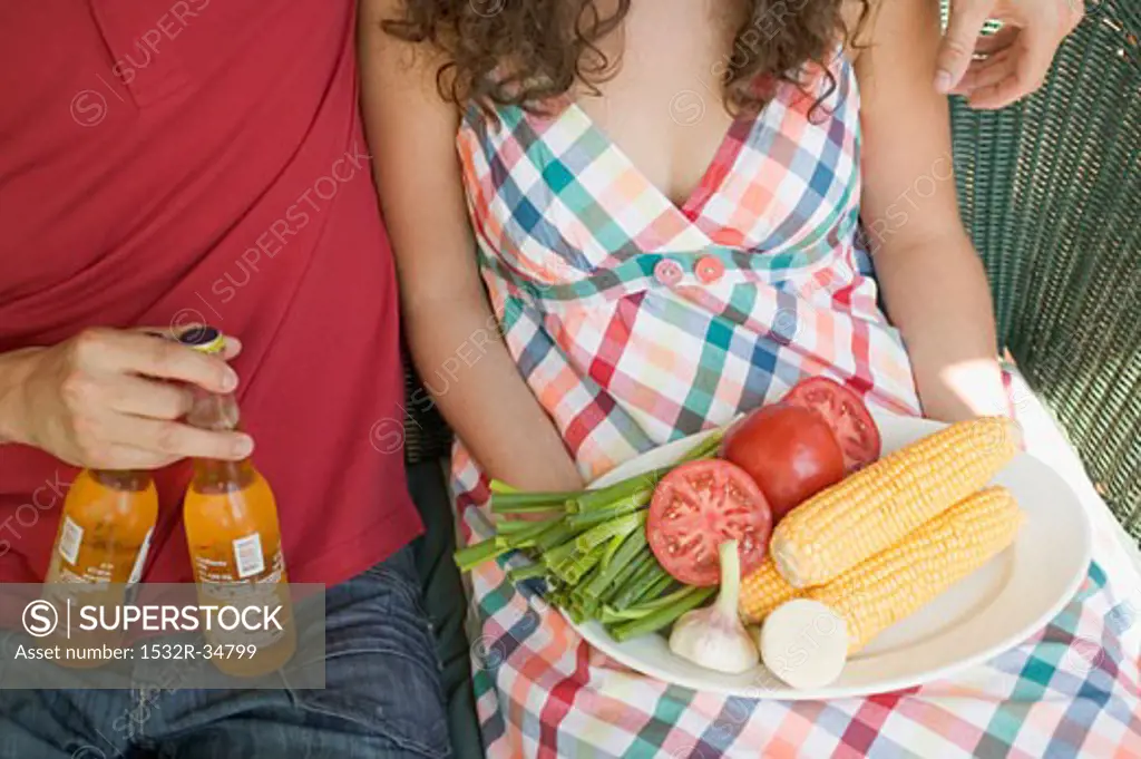 Seated couple with vegetables for grilling & bottles of beer