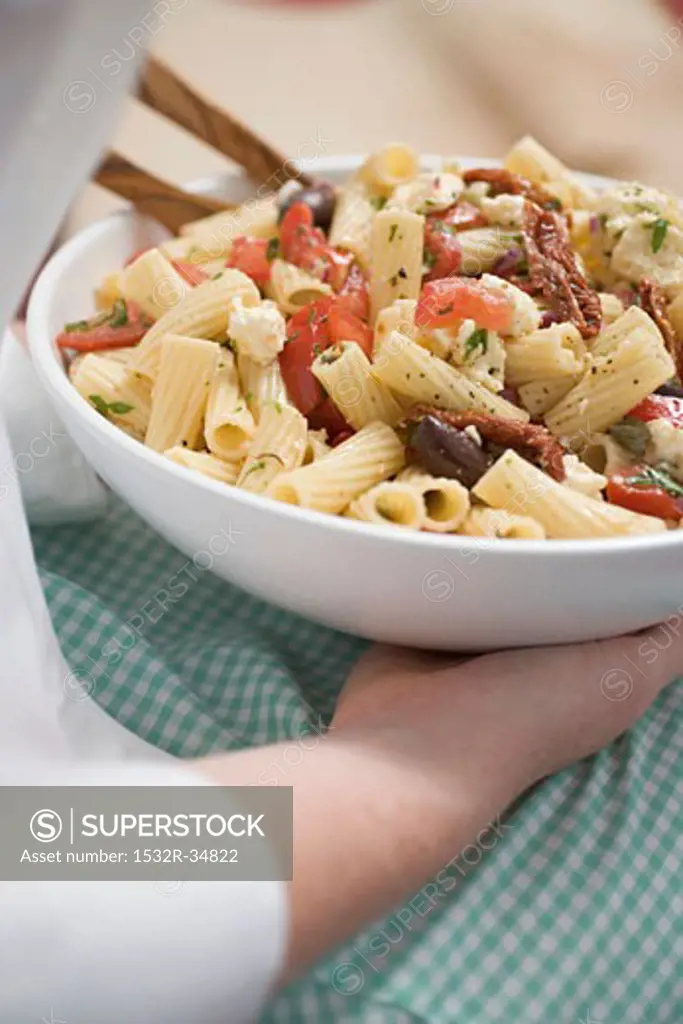 Woman holding dish of pasta salad with olives and tomatoes