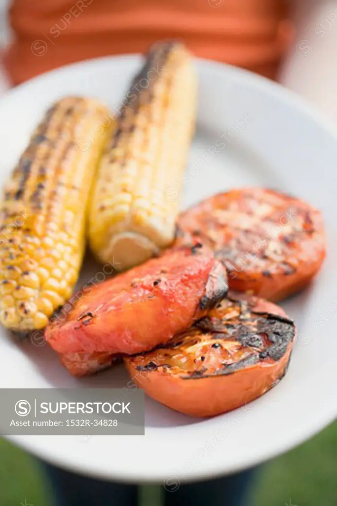 Person holding plate of grilled corn on the cob & tomatoes
