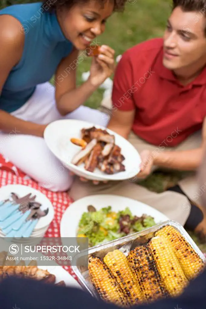 Couple with grilled spare ribs, corn on the cob, salad, on grass