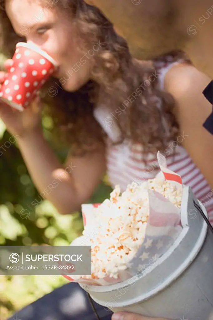 Woman drinking out of paper cup, man holding bucket of popcorn
