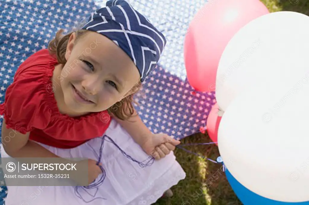 Small girl holding balloons in garden on the 4th of July