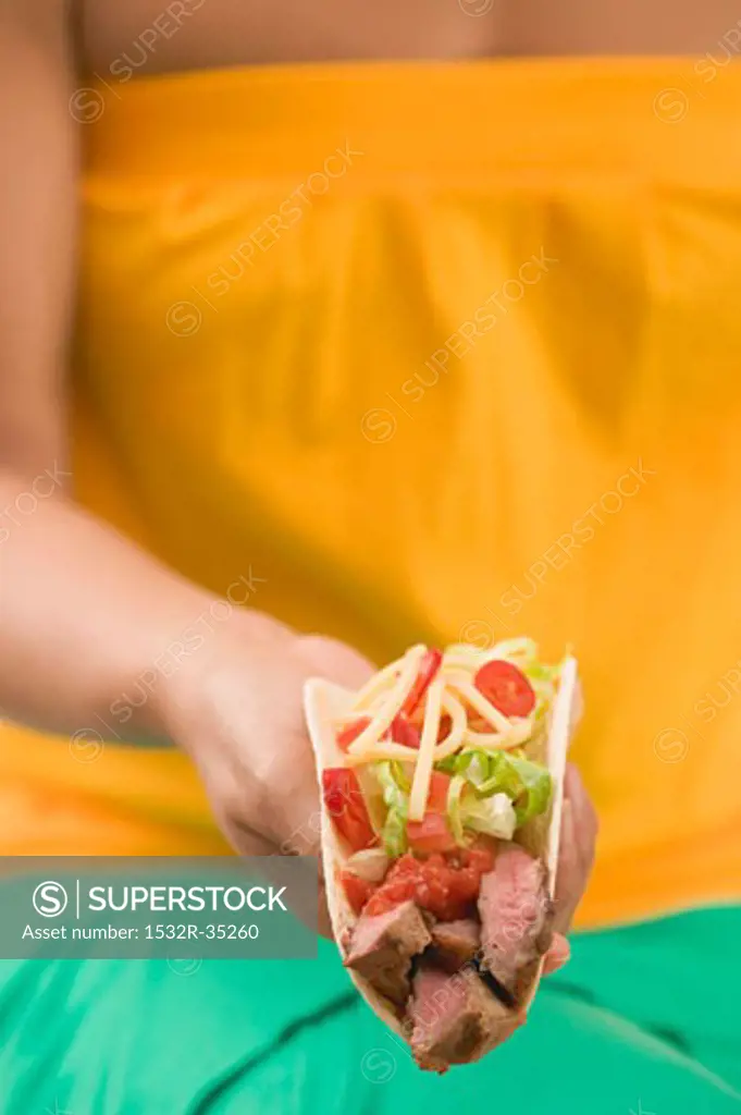Woman holding a taco filled with beef, salad and cheese