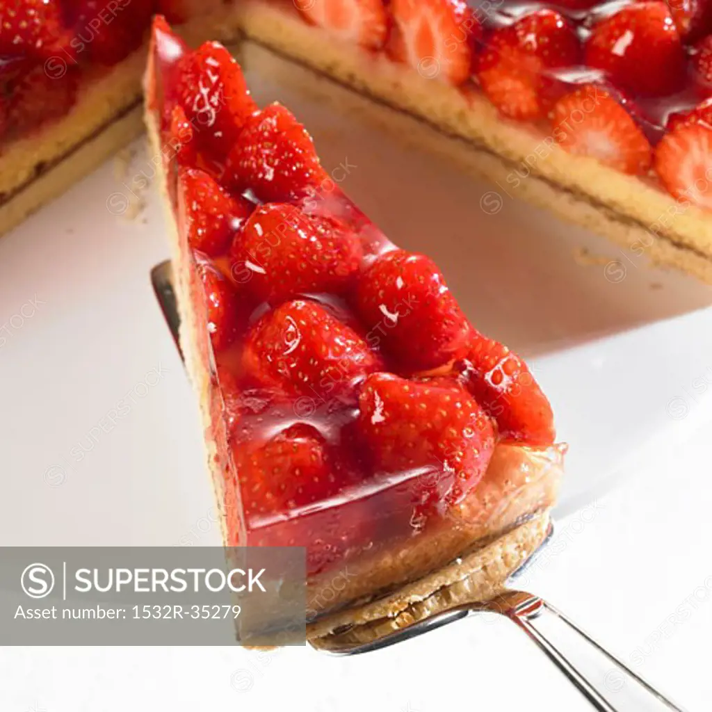 Piece of strawberry flan on server in front of remainder of flan