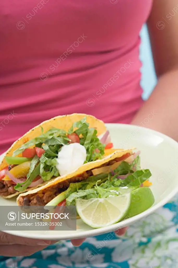 Woman holding plate with two tacos