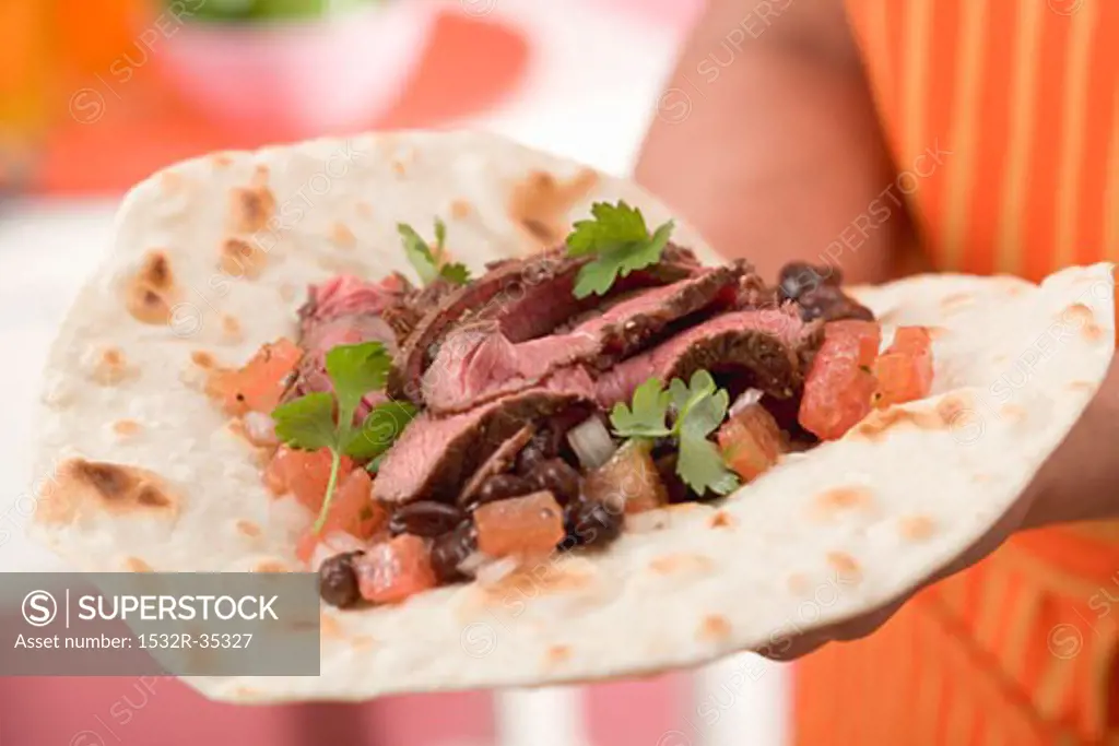 Woman holding fajita with beef, beans and tomatoes