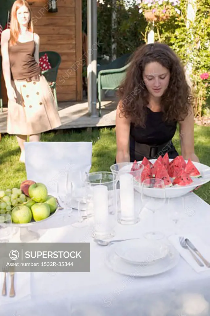 Woman carrying pieces of watermelon to table laid in garden