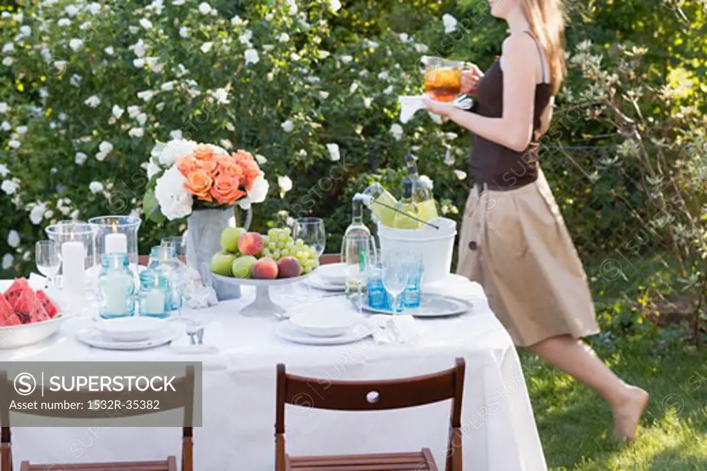 Woman bringing iced tea to table laid in garden