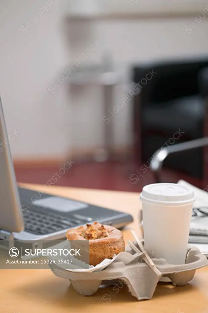 Muffin and cup of coffee beside laptop in office