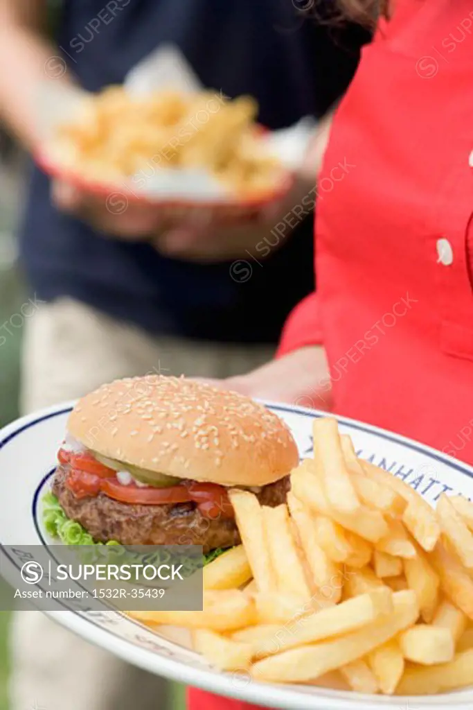 Woman holding plate of hamburger and chips