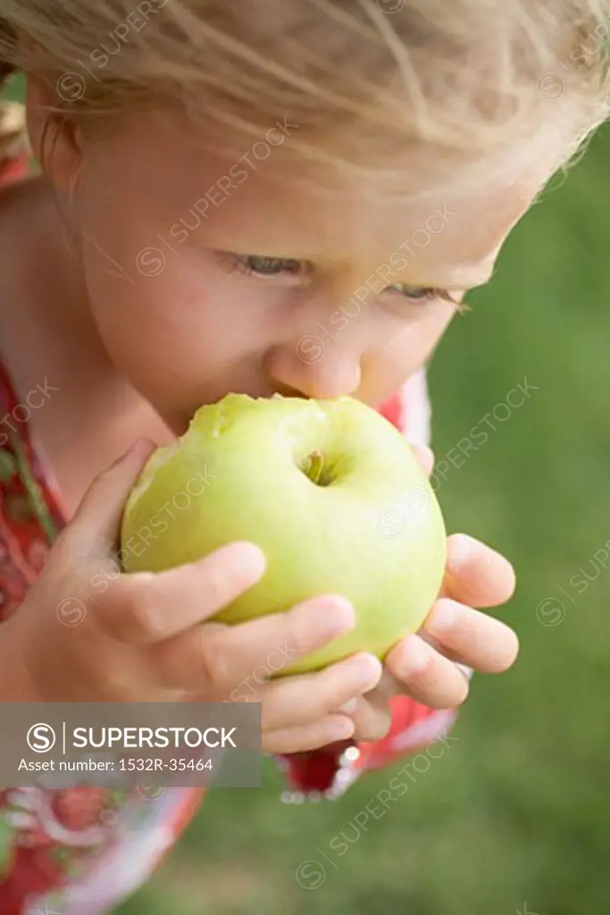 Small girl eating a large green apple