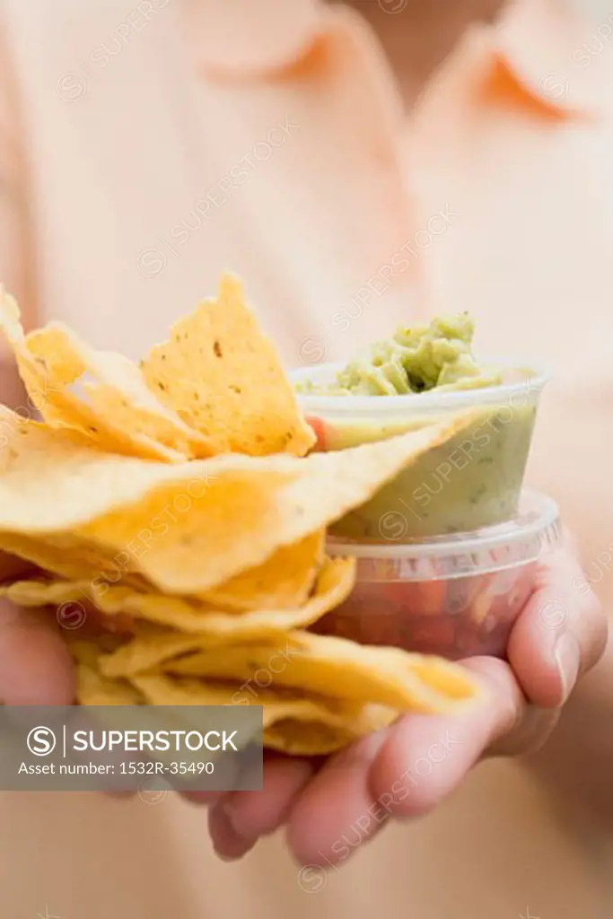 Woman holding plastic tubs of dips and nachos