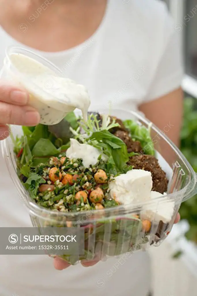Woman pouring dressing over salad in plastic container