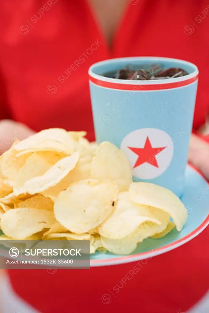 Woman holding crisps and beaker of cola on plate