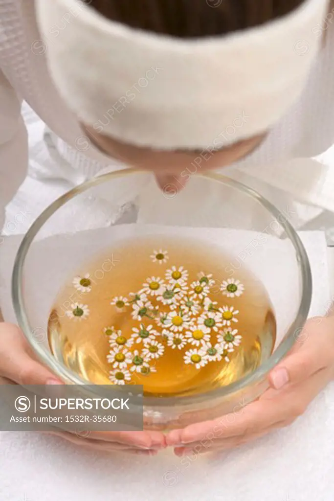 Woman bending over bowl of chamomile tea with flowers