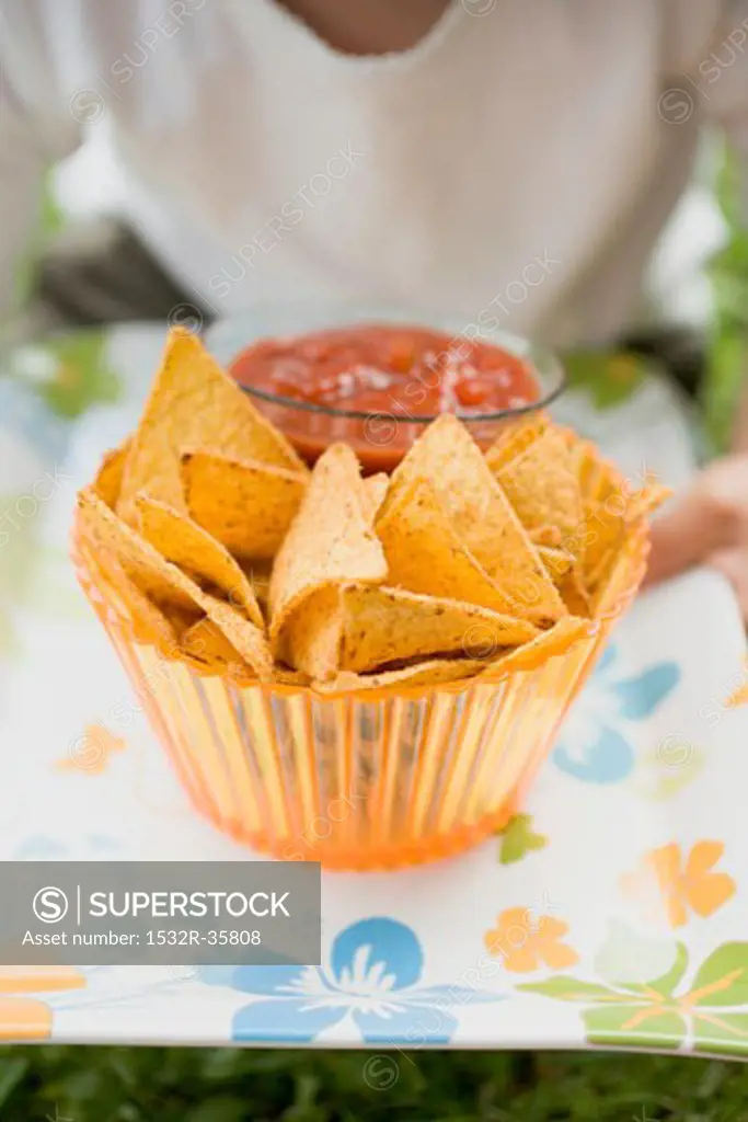 Child holding nachos and tomato salsa on tray