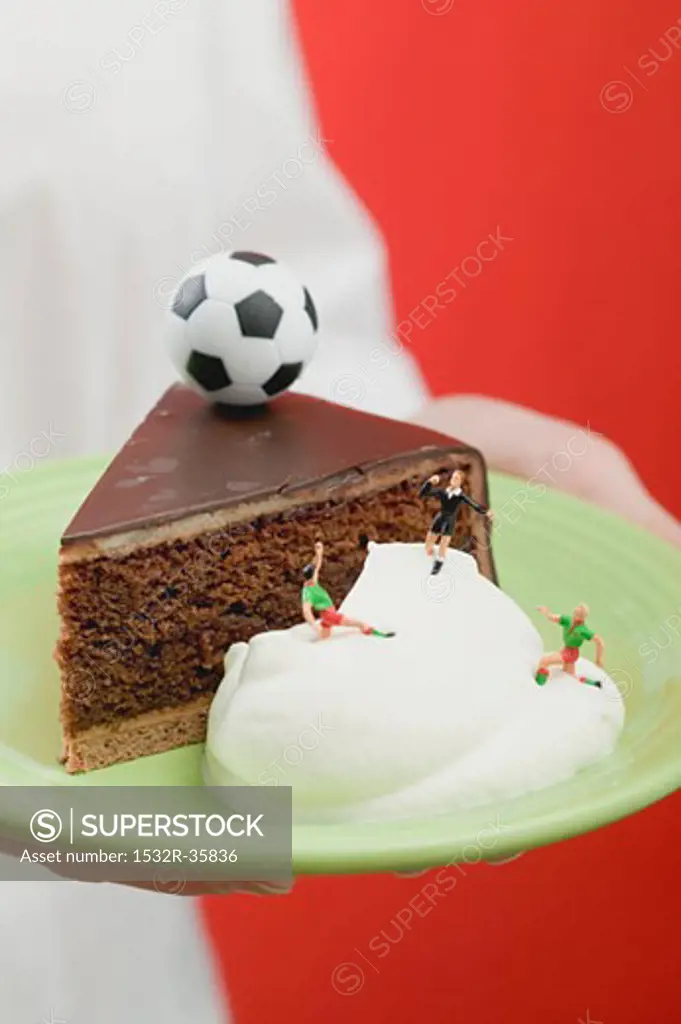 Person holding piece of Sacher torte with cream & football