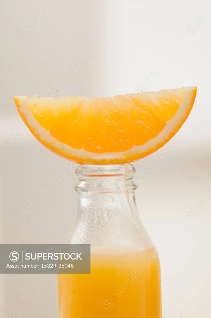Orange juice in bottle with fresh orange wedge