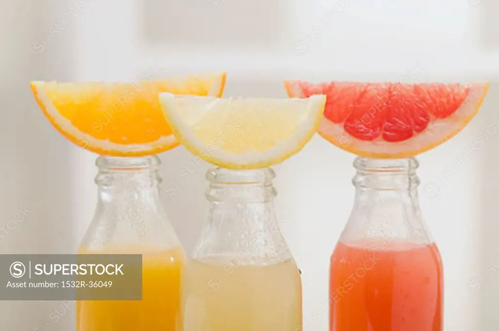Three fruit juices in bottles with wedges of fresh fruit