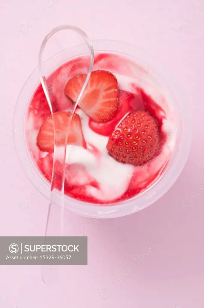 Strawberry yoghurt in plastic pot with spoon (overhead view)