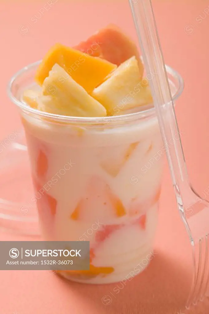 Yoghurt with fresh fruit in plastic pot, fork beside it