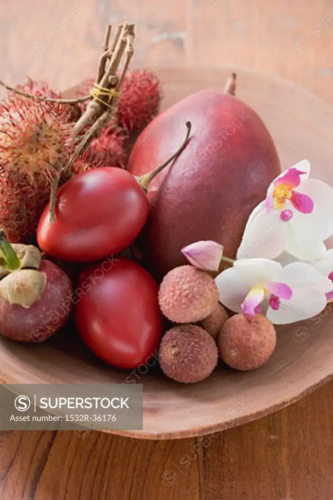 Assorted exotic fruits in a dish with orchids