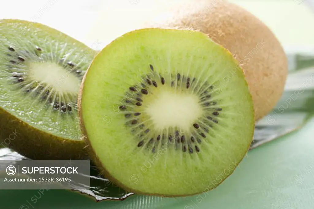 Two halves of a kiwi fruit in front of whole kiwi fruit